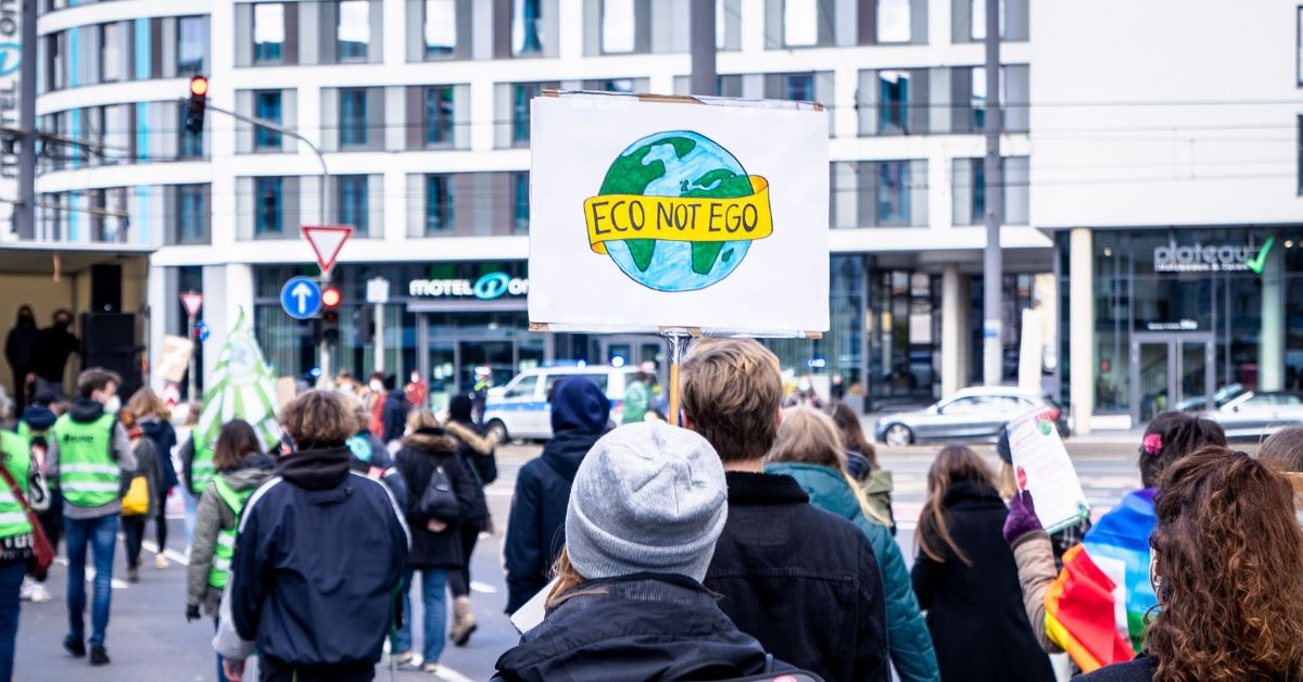 Picture of environmental activist holding a sign that says "eco not ego"